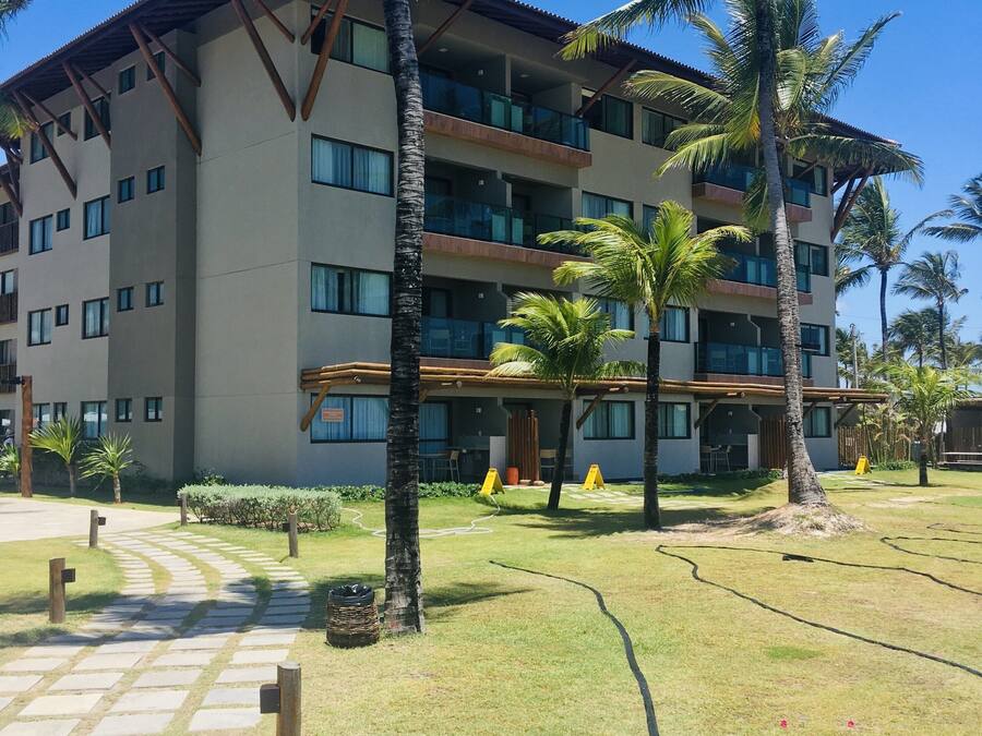 Un hotel de varios pisos con techo plano, amplias ventanas y un patio pavimentado con palmeras.
