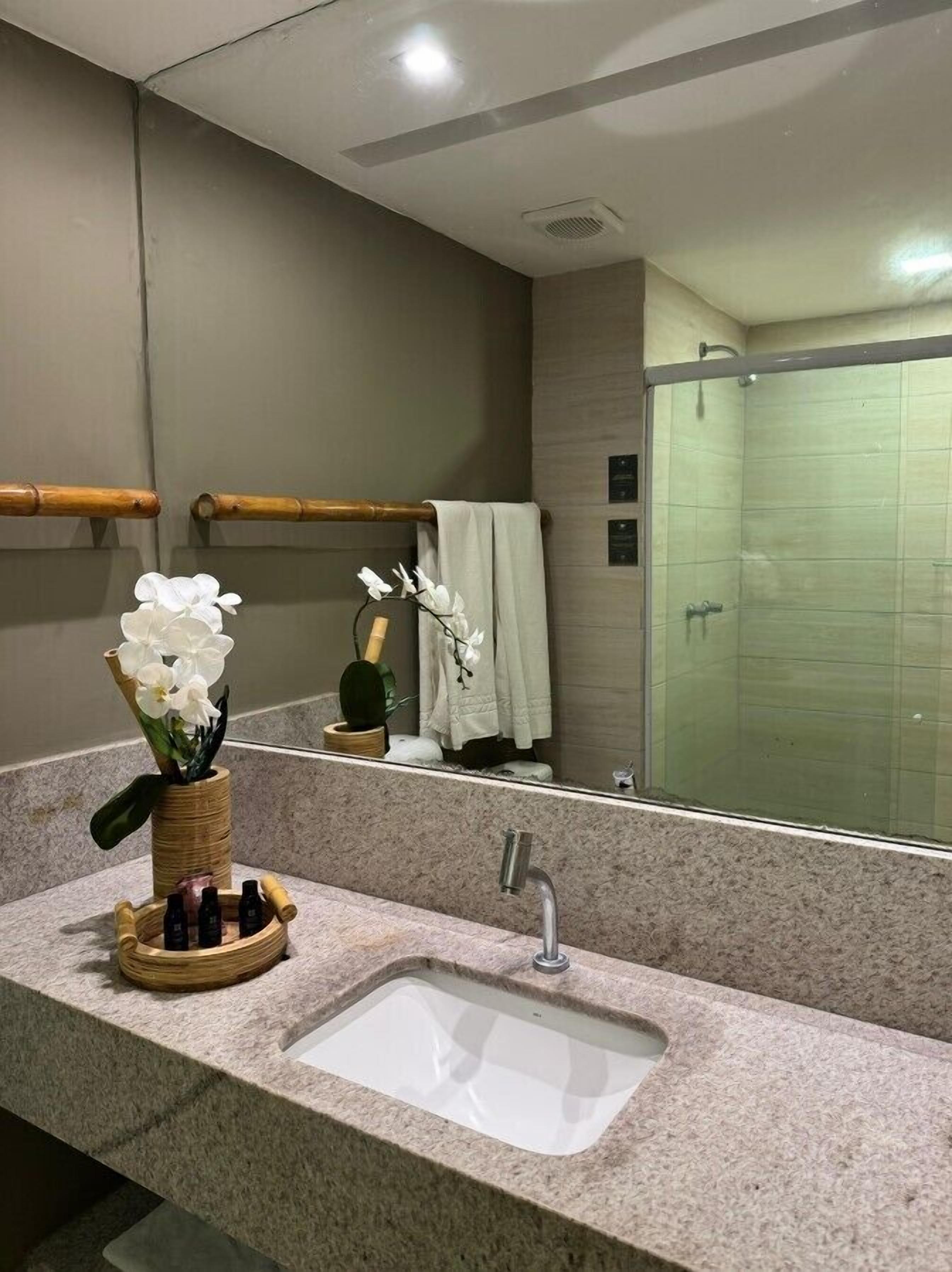 Un baño con encimera de granito, un lavamanos blanco, un espejo y una zona de ducha.