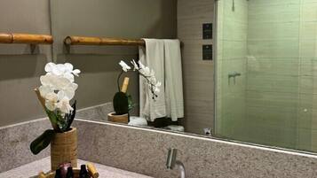 Un baño con encimera de granito, un lavamanos blanco, un espejo y una zona de ducha.