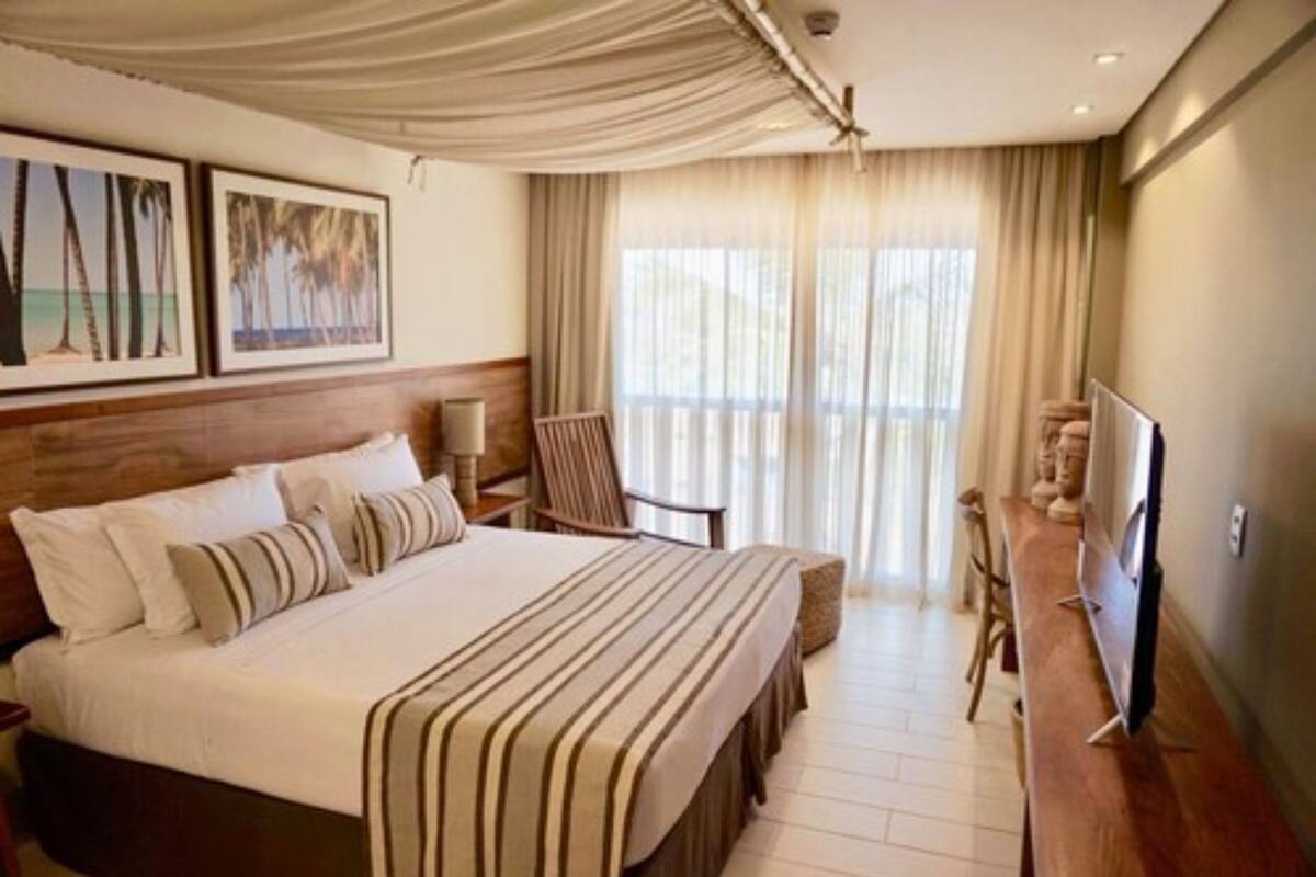 A hotel room with a large bed, a television, a desk, and a chair. There are curtains and a window.