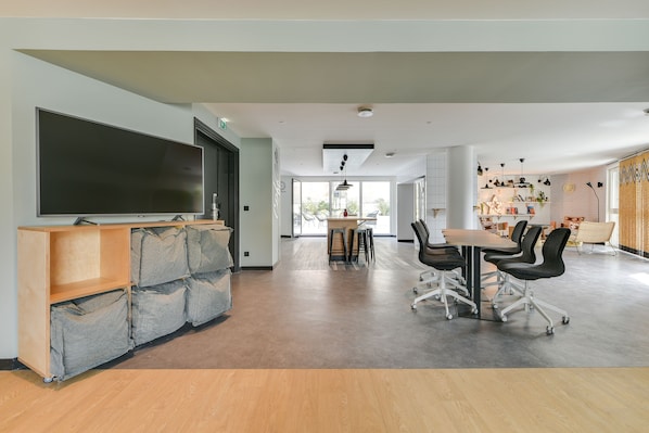Amplia sala de estar con un televisor de pantalla plana grande, un mueble de madera para entretenimiento, una mesa de comedor con sillas y una cocina al fondo.