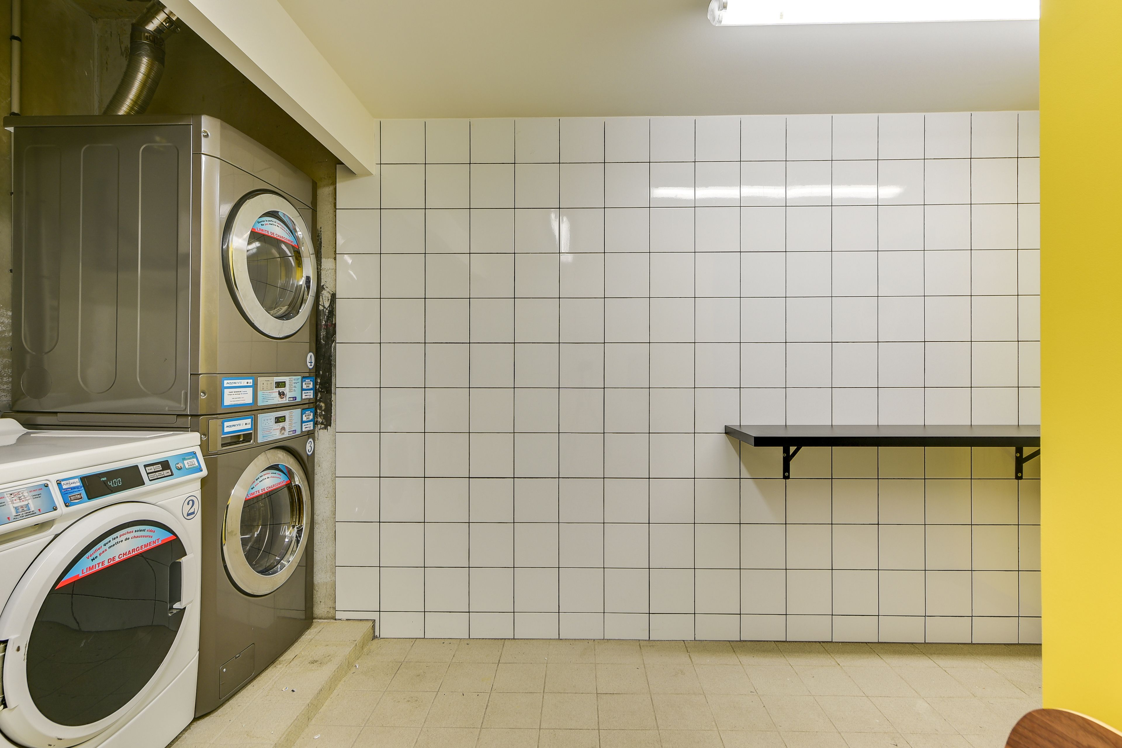 A laundry room with two washing machines, a bench, and tiled walls.