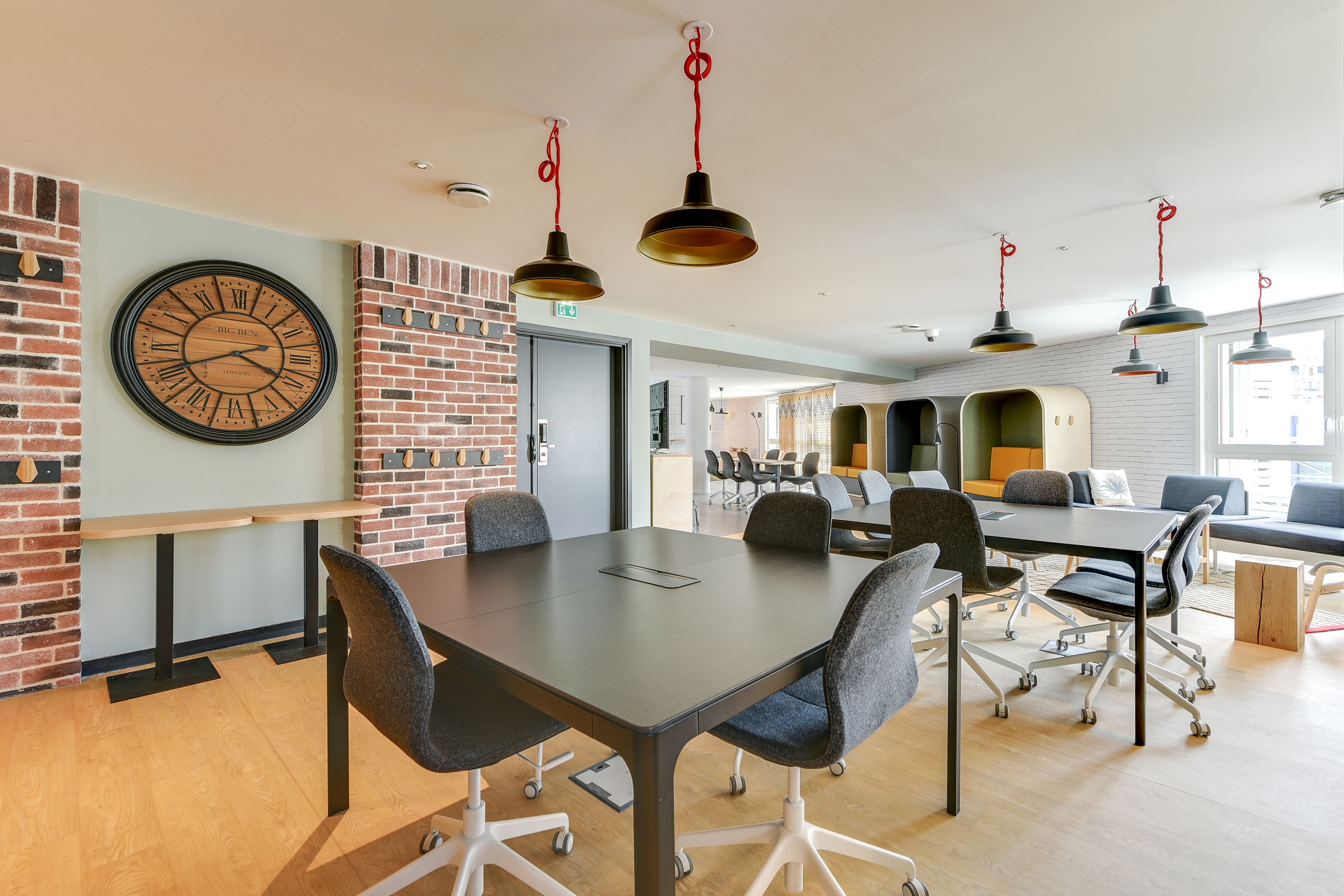 A modern meeting room with a large clock, brick walls, and a long table with chairs.