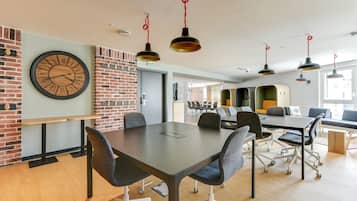 A modern meeting room with a large clock, brick walls, and a long table with chairs.