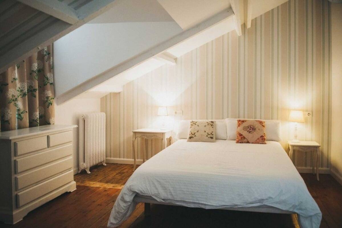 A bedroom with a large bed, two bedside tables, a dresser, and a radiator.
