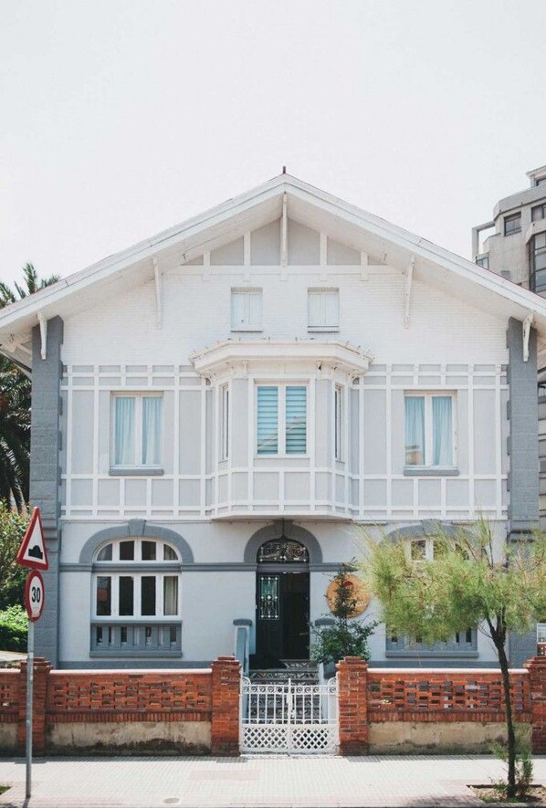 A two-story building with a white facade, a bay window, and a brick base. - Alamar Salinas - Hostel (Castrillon)