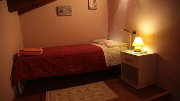 A small, cozy bedroom with a single bed, a bedside table with a lamp, and a small rug on the floor.