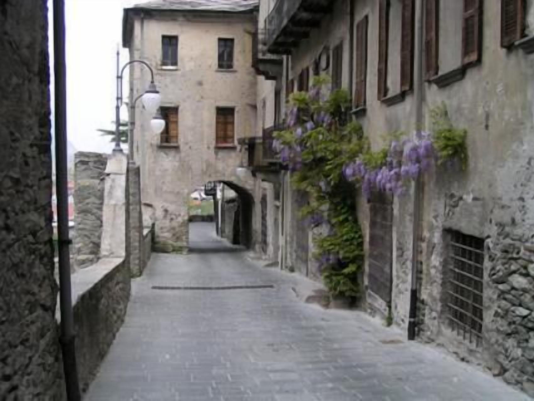 A narrow stone-paved street flanked by old buildings with arched doorways and wooden shutters.