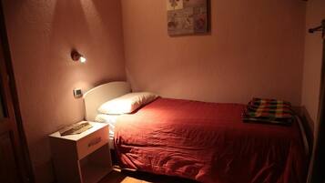 Ein kleines, gemütliches Schlafzimmer mit einem Einzelbett, einem Nachttisch und einer Wandleuchte.