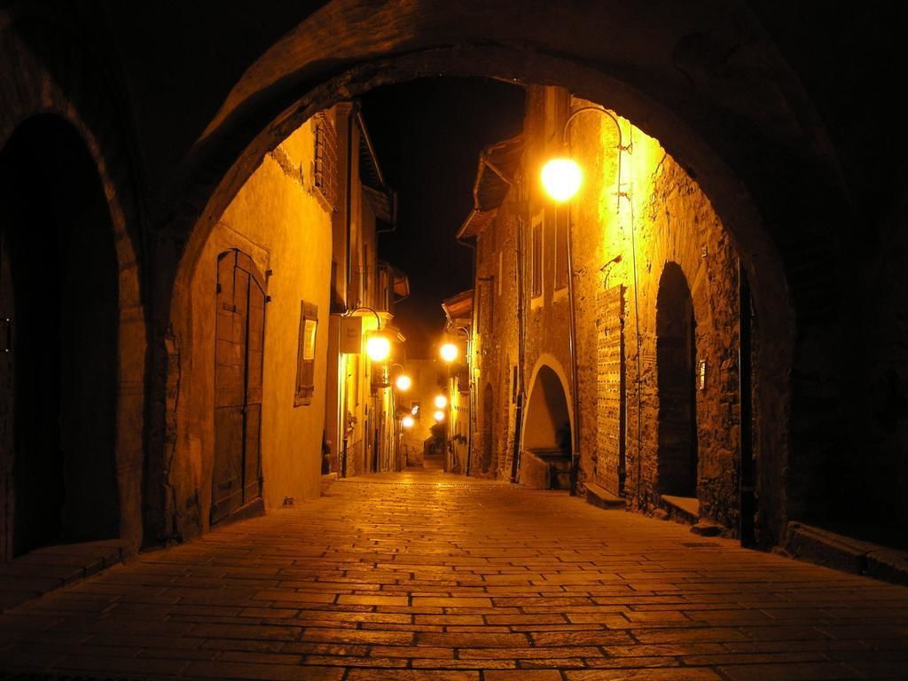 A narrow street with stone buildings and arched entrances, illuminated by warm lighting.