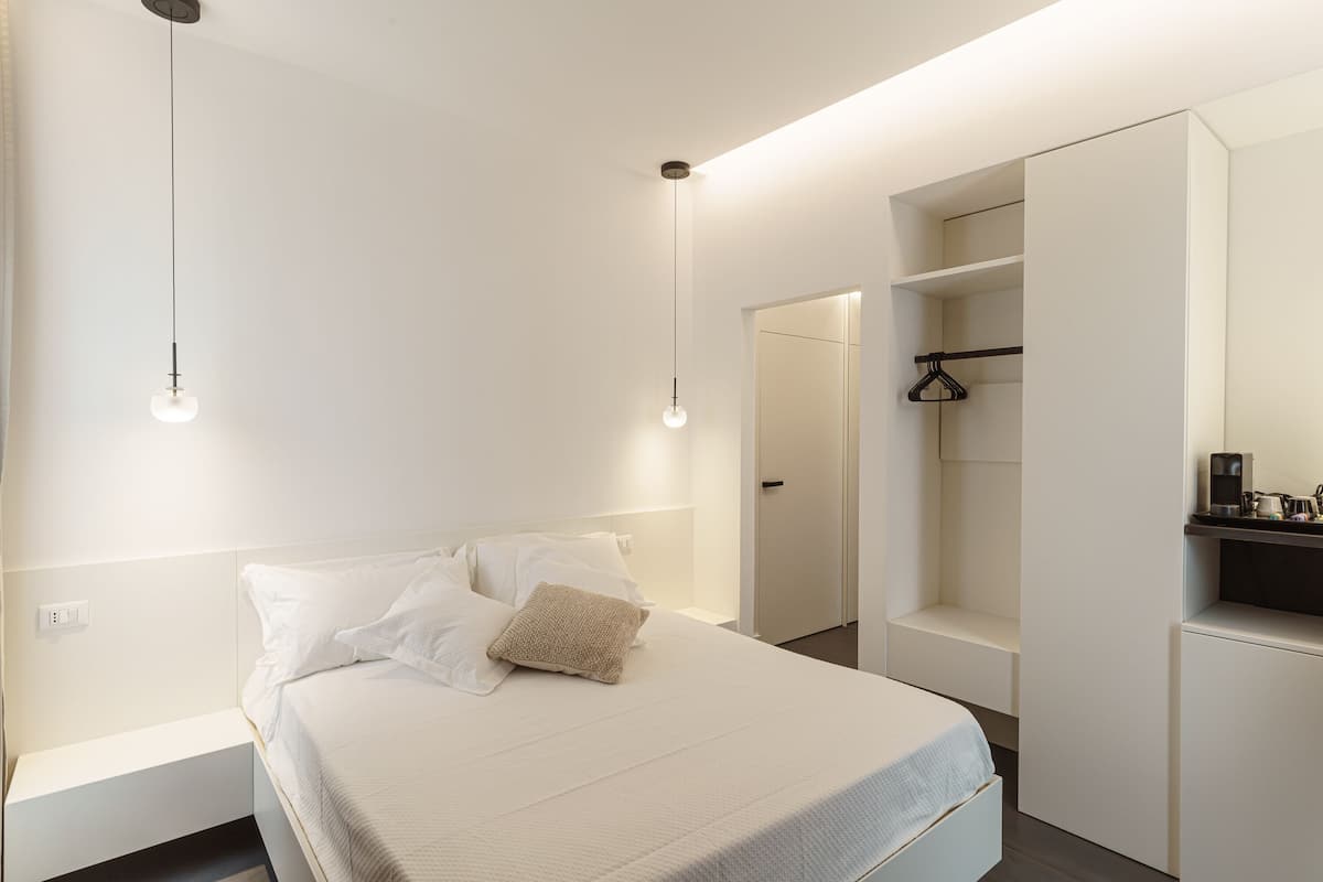 Une chambre moderne avec un lit bien fait, des tables de chevet, un luminaire suspendu et des rangements intégrés.