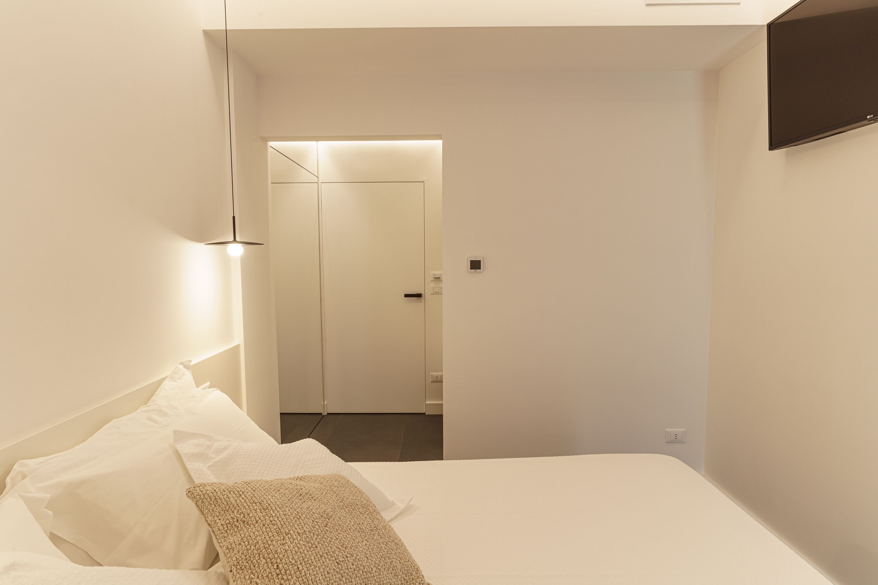 Quarto de hotel moderno com uma cama bem arrumada, uma televisão de tela plana na parede e uma porta que dá para o banheiro.