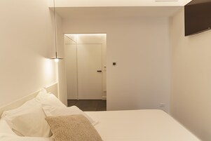 Quarto de hotel moderno com uma cama bem arrumada, uma televisão de tela plana na parede e uma porta que dá para o banheiro.