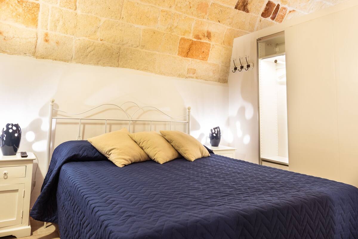 Une chambre à coucher avec un lit, une table de chevet, une commode et un mur en briques.