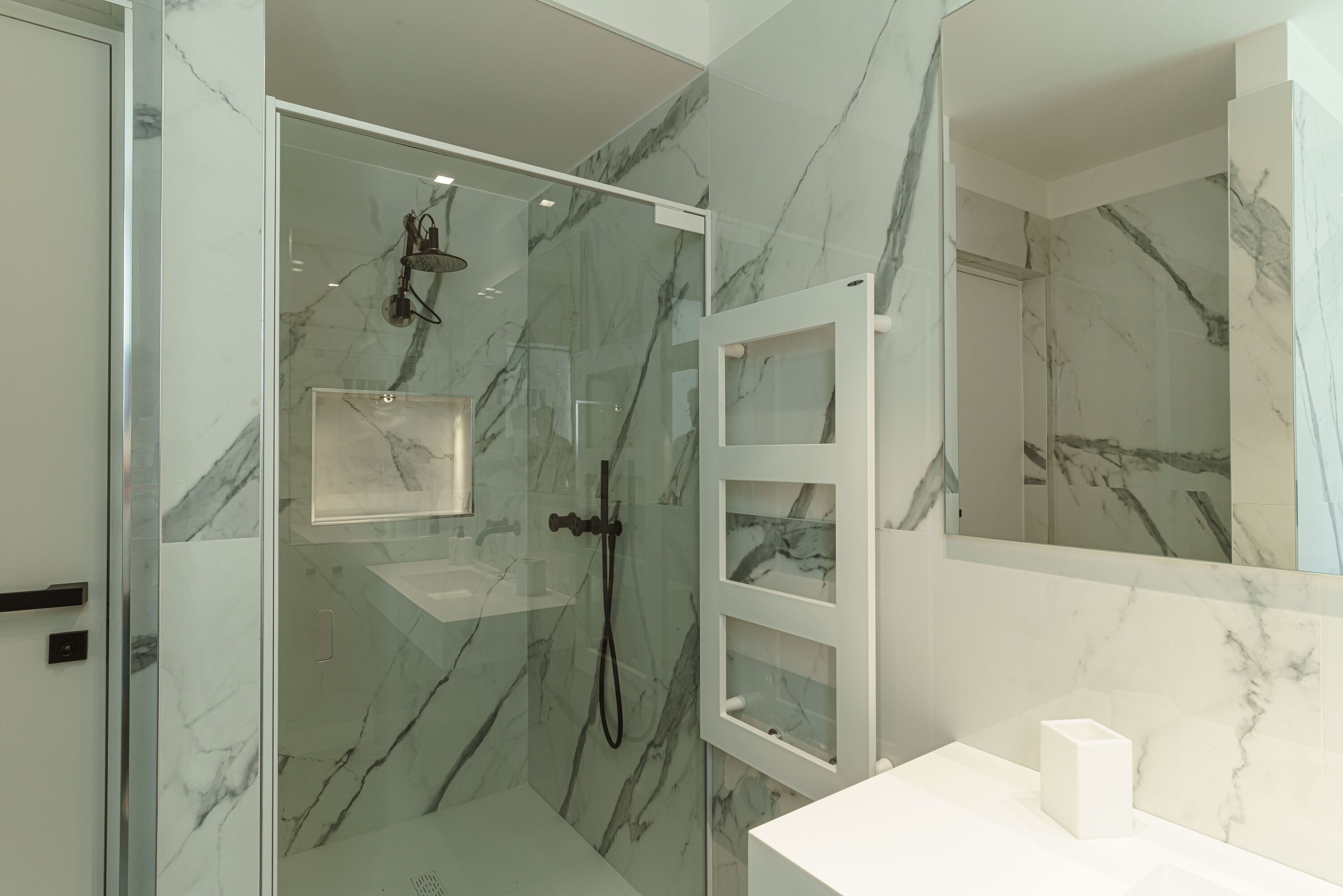 A modern bathroom with a glass-enclosed shower, marble walls, and a white vanity.