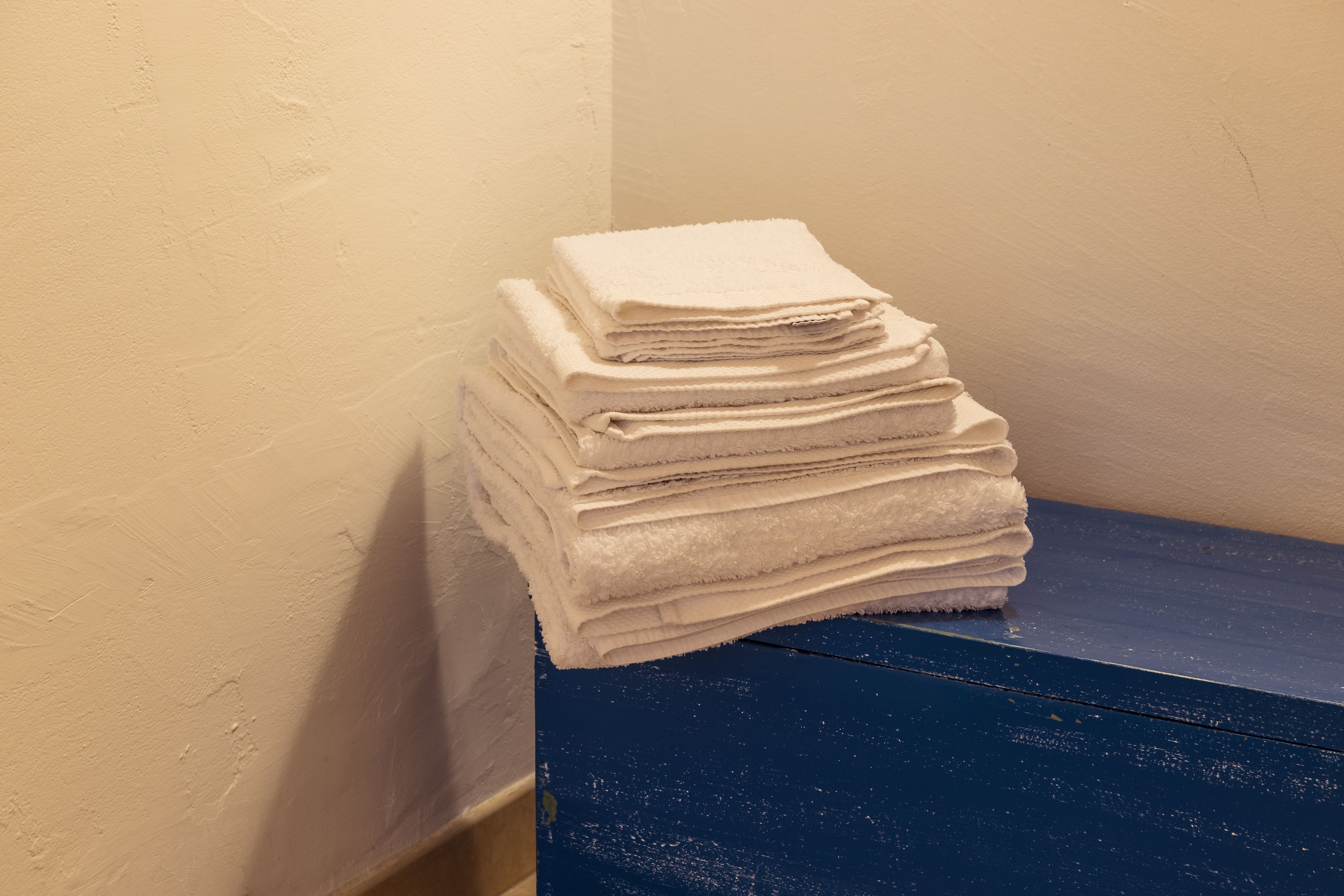 A stack of white towels on a blue surface against a beige wall.
