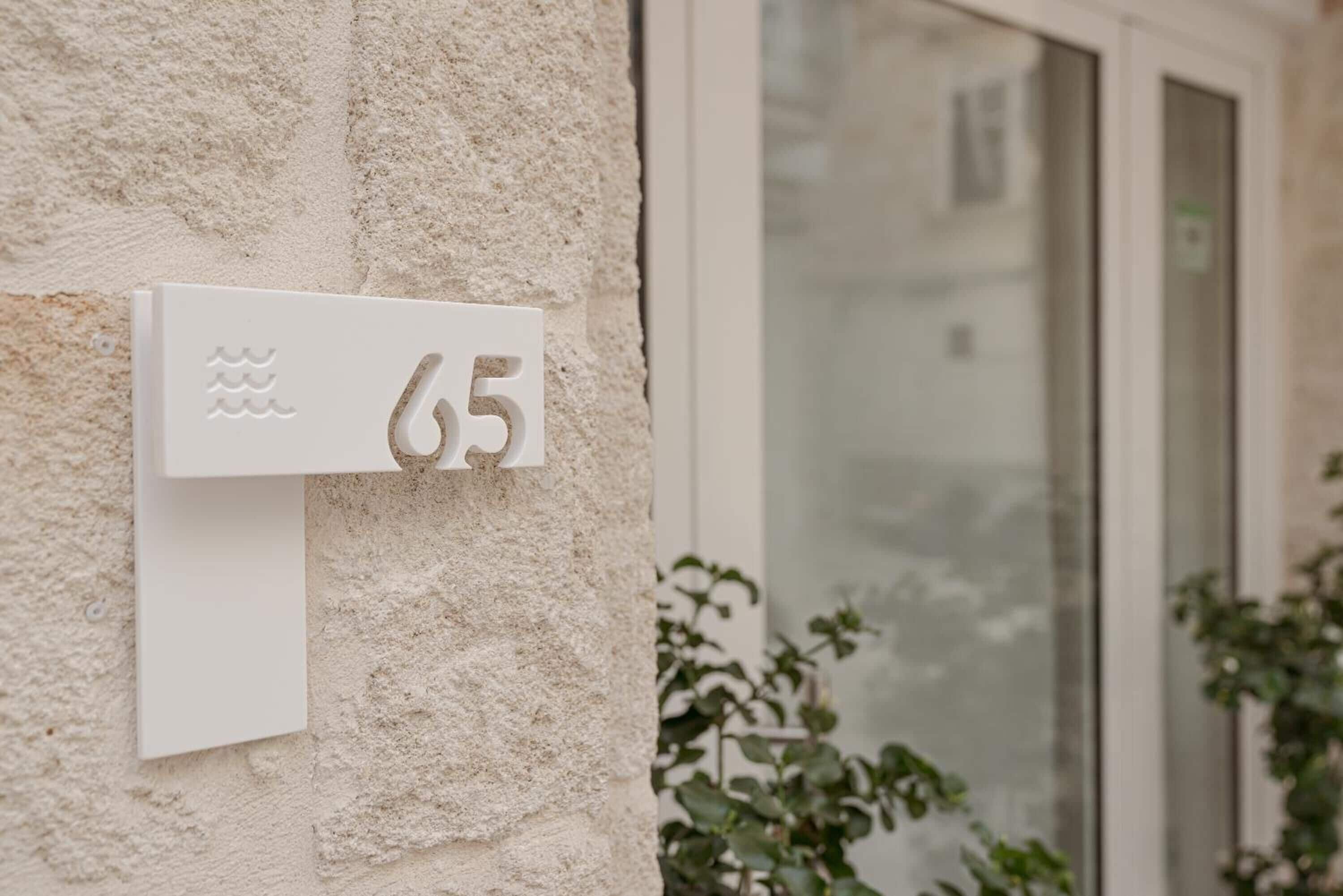 A house number '65' mounted on a textured stone wall.