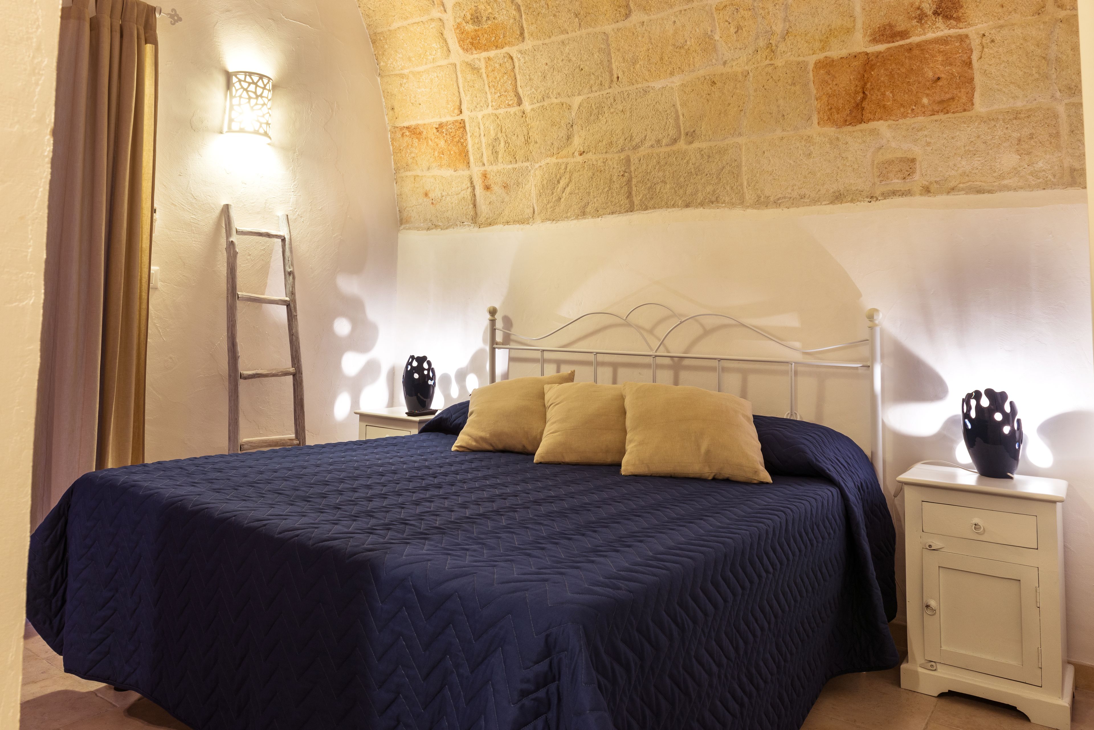 Ein Schlafzimmer mit einem Bett, einem Nachttisch, einer Wandlampe und einer Leiter.