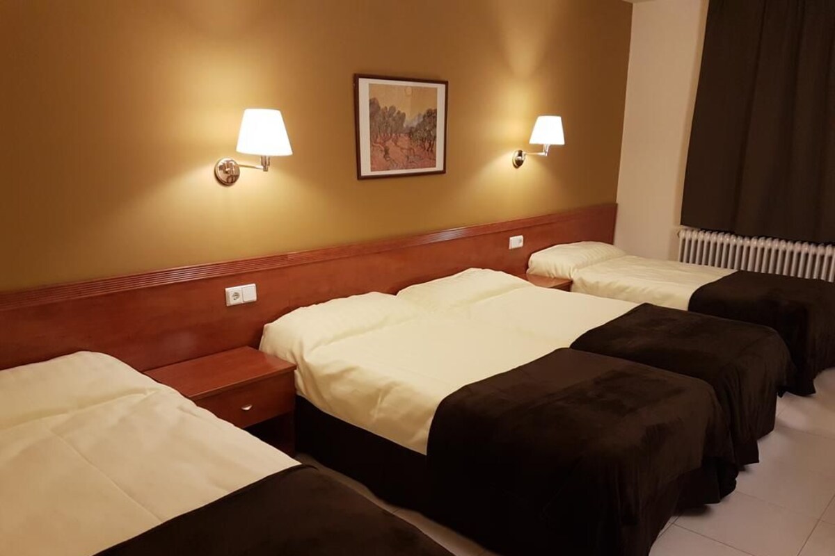 Una habitación de hotel con cuatro camas dispuestas en fila, cada una con cabecero y mesitas de noche.