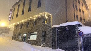 Un edificio histórico con fachada de piedra, un letrero del Hotel Guineu y nieve en el suelo.