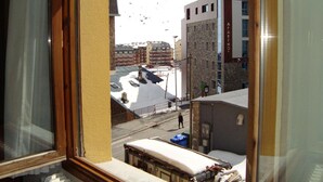 Vista desde una ventana con una montaña nevada al fondo, una calle con edificios y una persona caminando.
