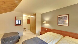 Habitación de hotel con dos camas, techo de madera, mesita de noche, lámpara, un cuadro y una puerta que da a otra habitación.