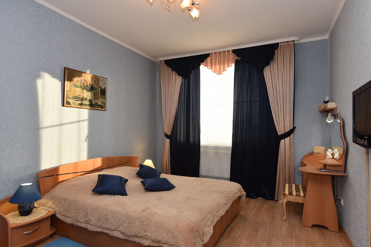 A bedroom with a bed, bedside table, lamp, and a desk with a chair.