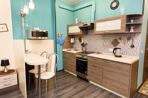 A compact kitchen with a microwave, oven, and sink. There are wooden cabinets and a tiled backsplash.