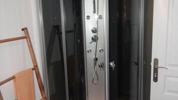 Cabina de ducha con mampara de vidrio, cabezal de ducha manual y rociador de mano.