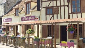 Un edificio tradicional con entramado de madera y madera expuesta, con un letrero de restaurante, mesas al aire libre y macetas de flores colgantes.