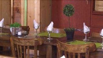 A wooden interior with tables and chairs, each with a green table runner and a white napkin.