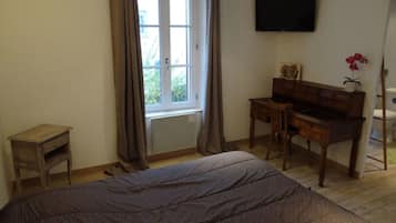 Un dormitorio con cama, escritorio, silla, televisor y ventana con cortinas.