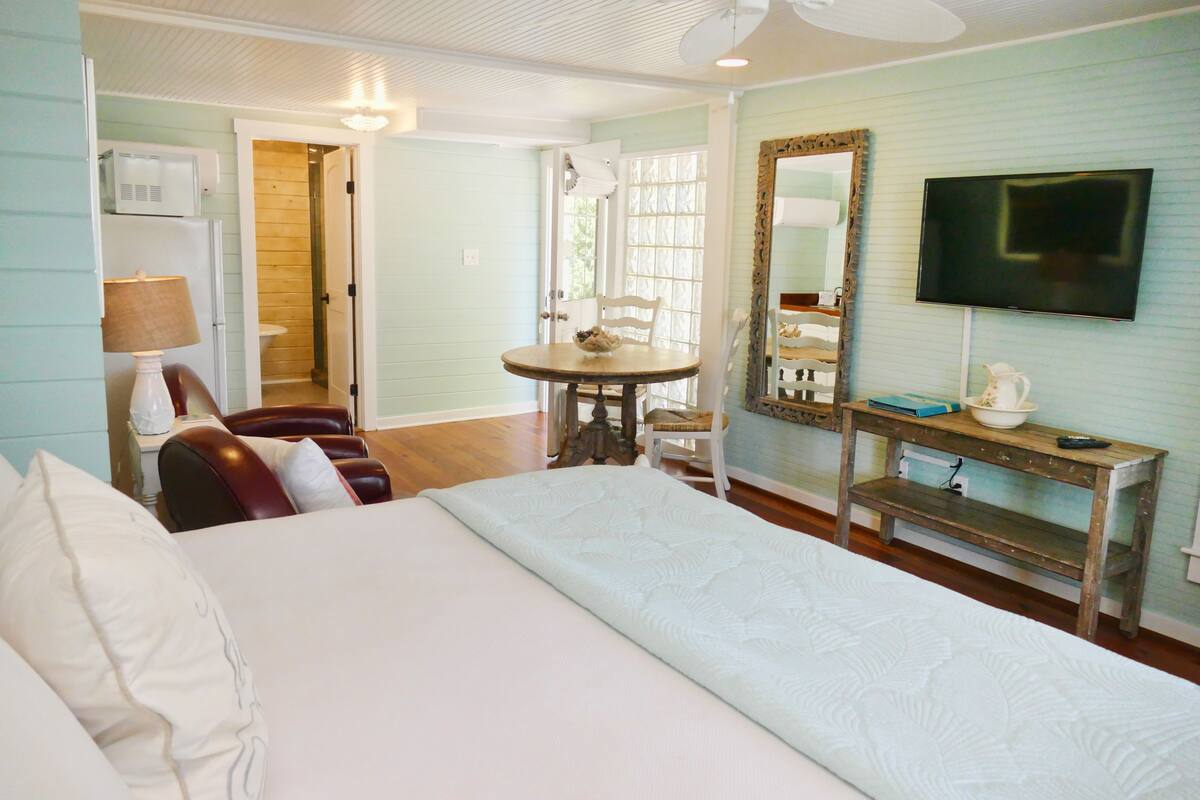 A hotel room with a large bed, a wooden table with chairs, a television, and a mirror on the wall.