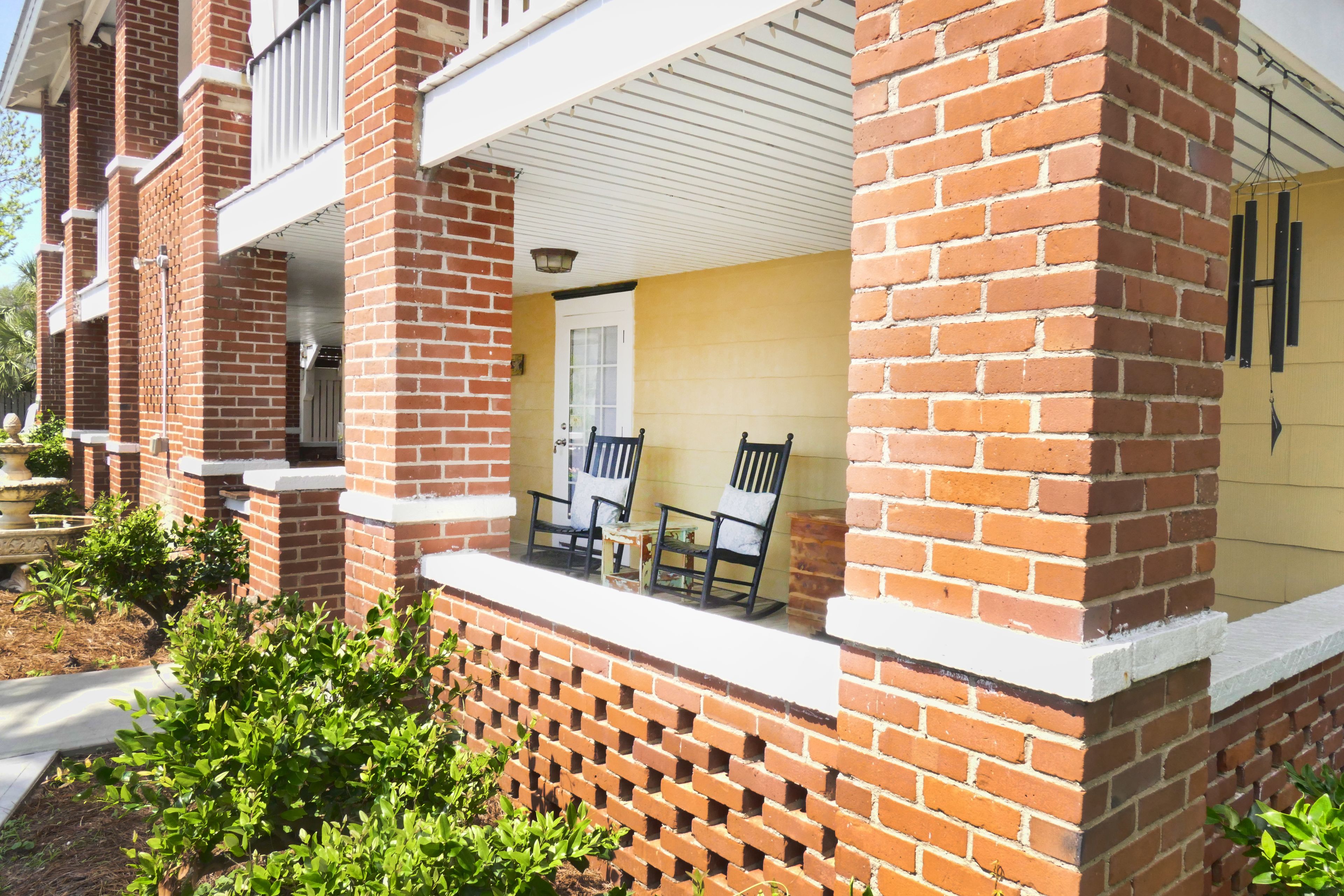 A brick building with a porch, two chairs, and a door.