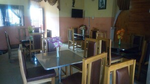 A dining area with wooden chairs and tables, a vase with flowers, and a clock on the wall. - Blue Banana Resorts (Abeokuta)
