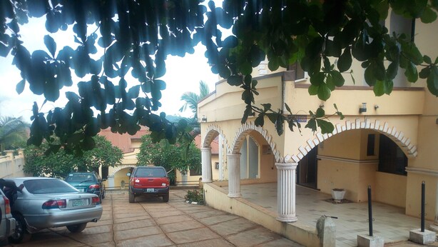 A residential area with parked cars, a house with a yellow facade, and a covered entrance with white columns. - Blue Banana Resorts (Abeokuta)