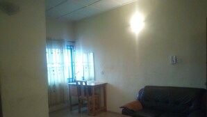 A living room with a sofa, a wooden coffee table, a dining table with chairs, and a window with curtains. - Blue Banana Resorts (Abeokuta)