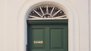 A green door with a nameplate, a brass doorknob, and a decorative metal crest above it. - Casa Meliò (Polignano a Mare)