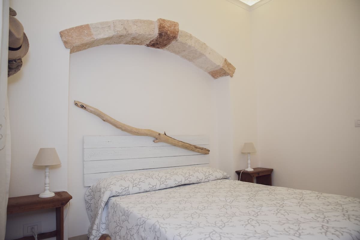 A bedroom with a bed, two bedside tables, a lamp on each, a stone arch above the bed, and a branch on the wall.