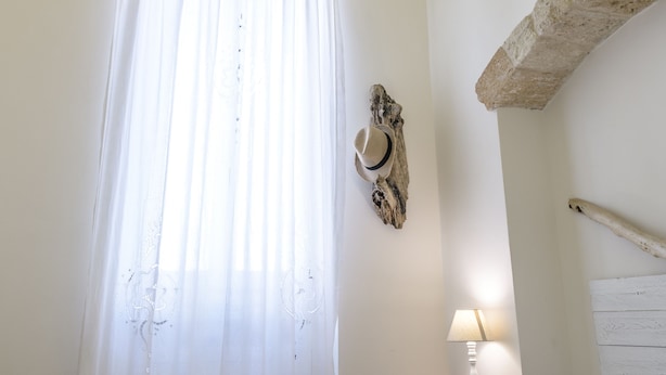 A bedroom with a stone ceiling, a bed with a patterned bedspread, a nightstand with a lamp, and a rustic wall decor piece. - Casa Meliò (Polignano a Mare)