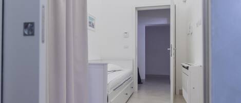 A narrow hallway with a bed, a desk, and a cabinet.