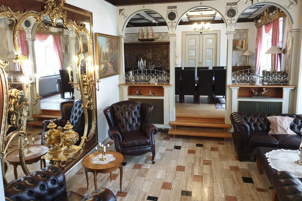 A luxurious room with ornate furniture, a grand mirror, and a dining area with a chandelier.