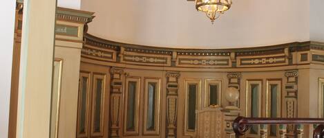 A room with ornate moldings, a chandelier, and a chair.