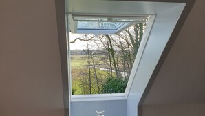 A skylight window with a white vase and a doily on a shelf, overlooking a landscape with trees and a building. - Gørdinglund Herregård Mainbuilding (Gording)