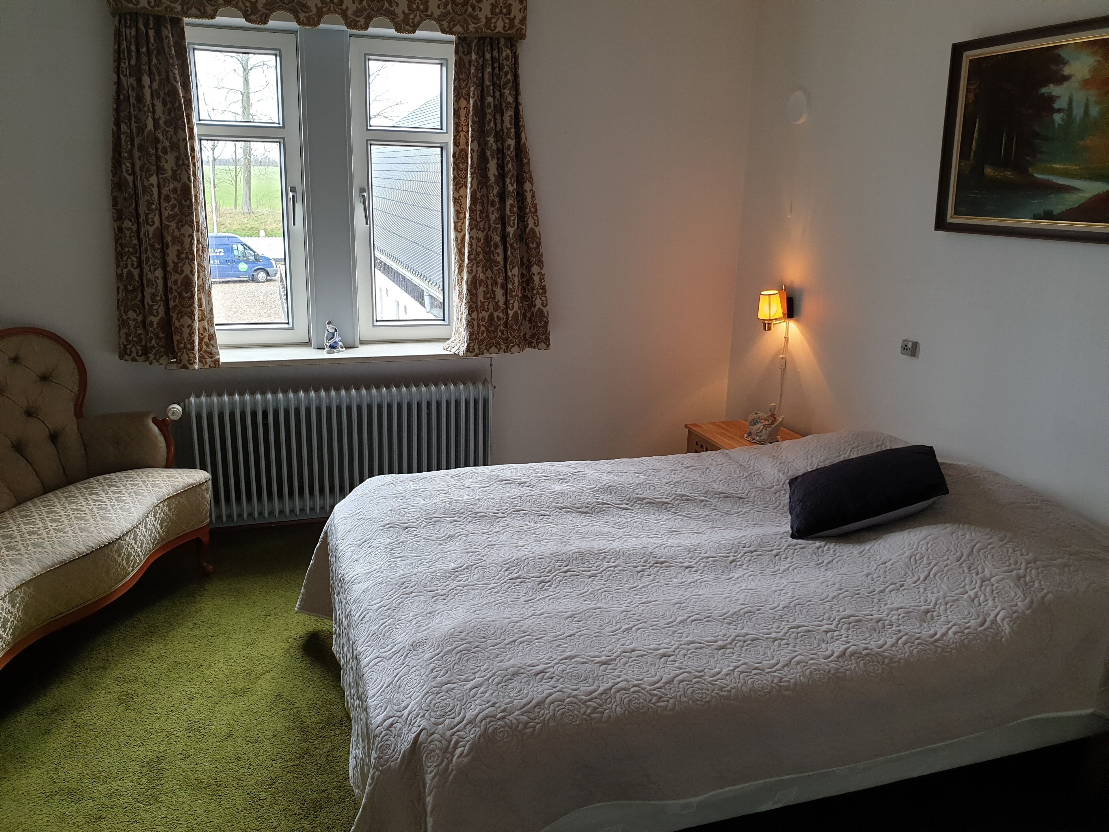 Une chambre avec un grand lit, une chaise, un radiateur et une fenêtre avec des rideaux.
