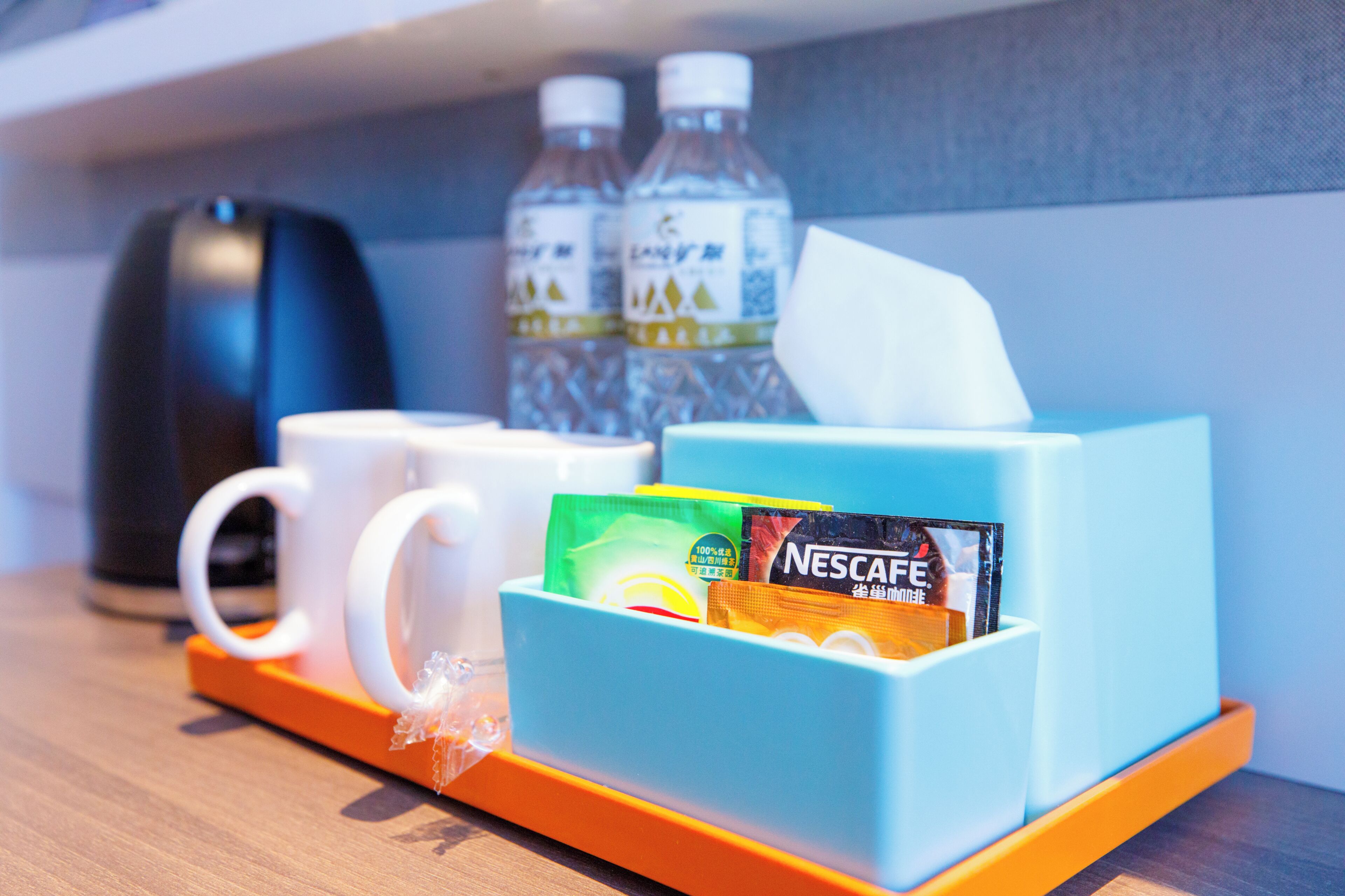 A hotel room's breakfast area with a coffee maker, two water bottles, a tissue box, and a Nescafe coffee packet.