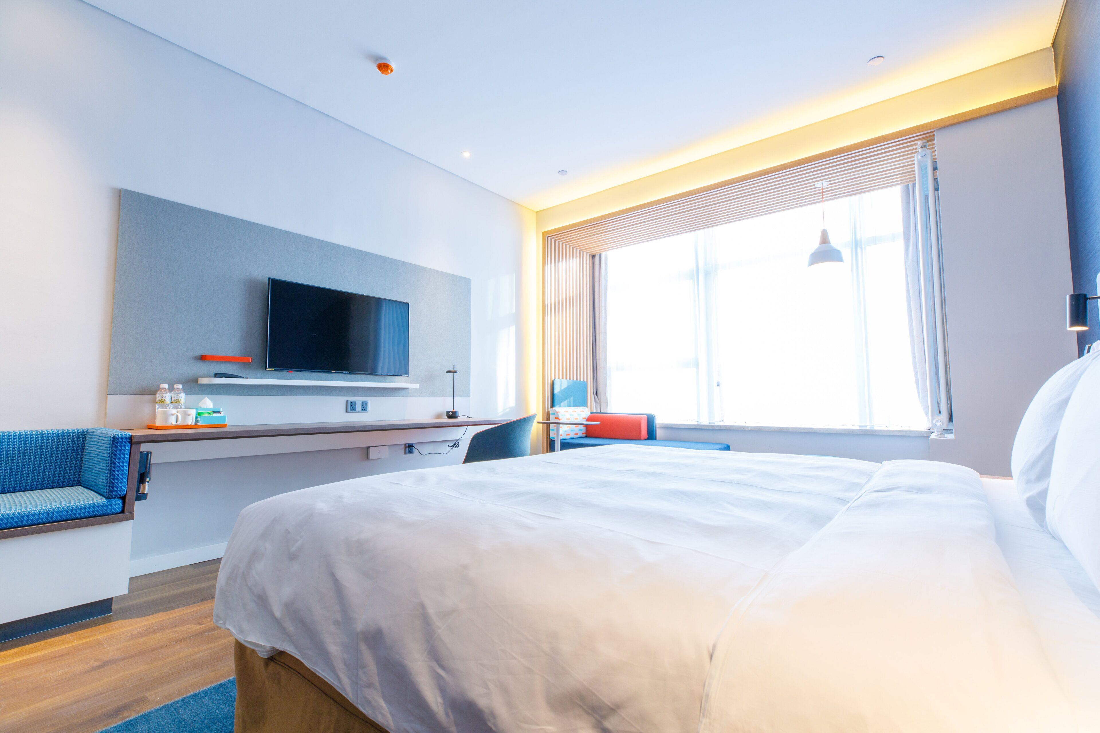 Ein Hotelzimmer mit einem Bett, einem Schreibtisch, einem Fernseher und einem Fenster mit Vorhängen.
