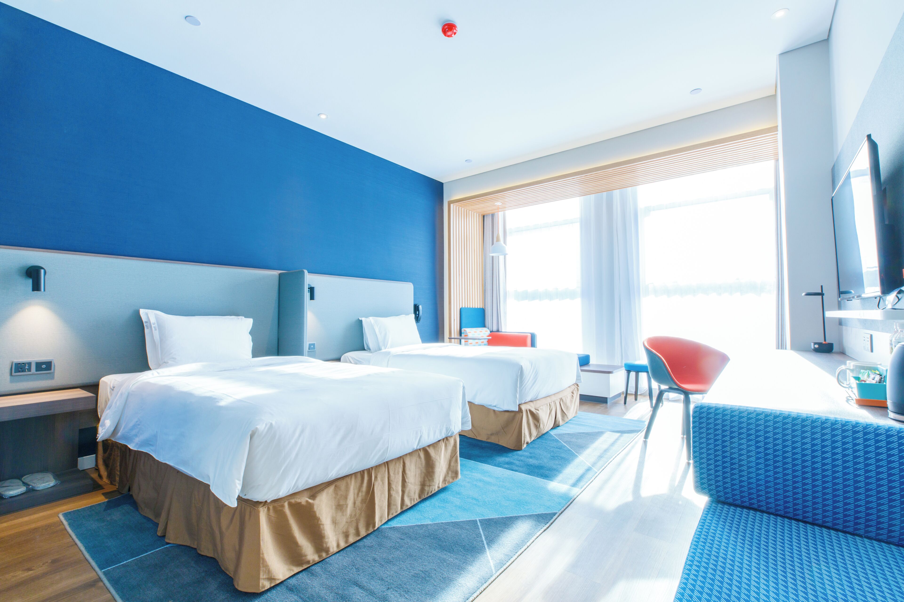 A hotel room with two beds, a desk, a chair, and a TV.