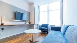 A modern living room with a flat-screen TV, a round white table, a blue sofa, and a blue armchair. - Holiday Inn Express Harbin Qunli by IHG (Harbin)