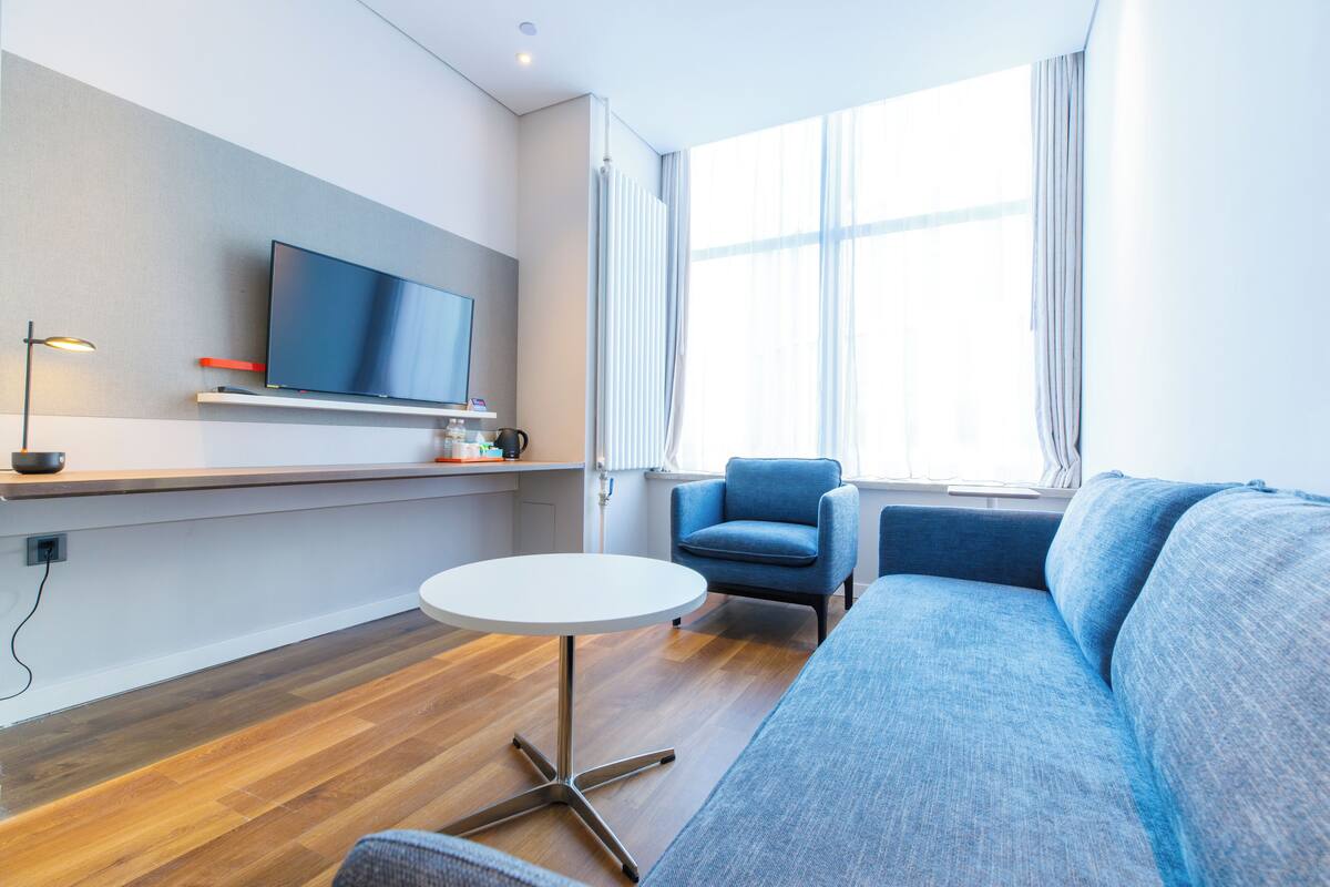 Un salon moderne avec un téléviseur à écran plat, une table ronde blanche, un canapé bleu et un fauteuil bleu.